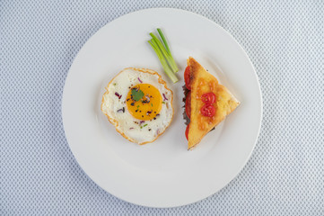 Fried egg on a white plate with sliced ​​Spring onion and sliced ​​tomatoes