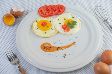 Fried egg on a white plate with sliced ​​Spring onion and sliced ​​tomatoes