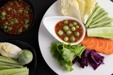 Shrimp-paste sauce in a bowl on the white plate with cucumber, yard long bean, thai eggplant, fried white cabbage, carrots and salad