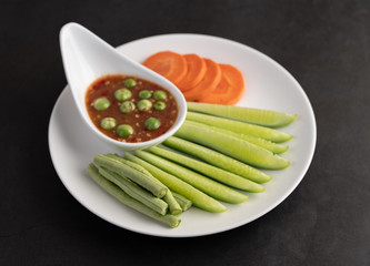 Shrimp-paste sauce in a bowl on the white plate with cucumber, yard long bean and carrots.