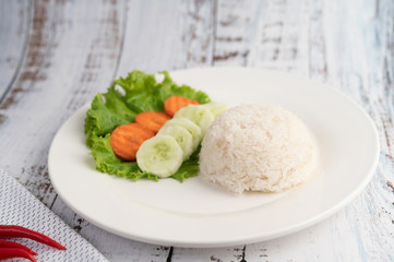 Steamed rice on a plate with cucumber, salad and carrots.