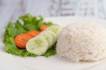 Steamed rice on a plate with cucumber, salad and carrots.