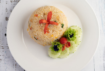 Fried rice with eggs in a white plate on wood background.