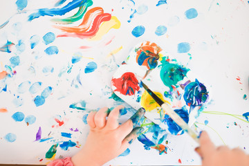 A child is painting with fingers and brush and oil paints