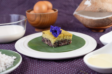 Black sticky rice and custard on a banana leaf in a white plate with butterfly pea flowers.