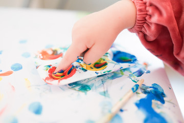 A child is painting with fingers and brush and oil paints