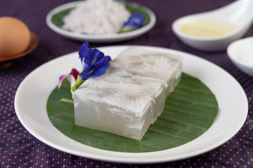 Coconut jelly is placed on a banana leaf in a white dish with butterfly pea flowers and with orchids.