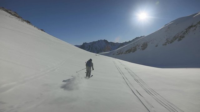 free ride off-piste skier skiing in fresh deep powder snow skiing towards the sun with an amazing blue sky and mountain view
