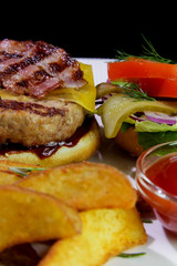 Unhealthy food.Burger with fried bacon, french fries, vegetables and ketchup on a white plate.Close-up