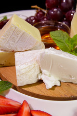 Camembert cheese served with strawberries, mint, grapes, honey on a white plate.Cheese plate