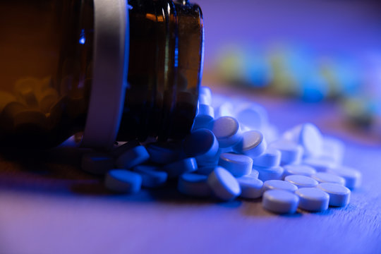 Opioids in a glass bottle. Opioid epidemic. Tablets and pills under blue light. Closeup of medicinals and pain killers.