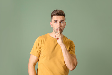 Young man showing silence gesture on color background