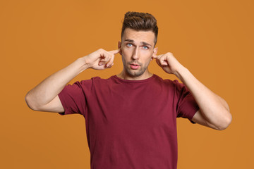 Fototapeta premium Young man closing ears with hands on color background