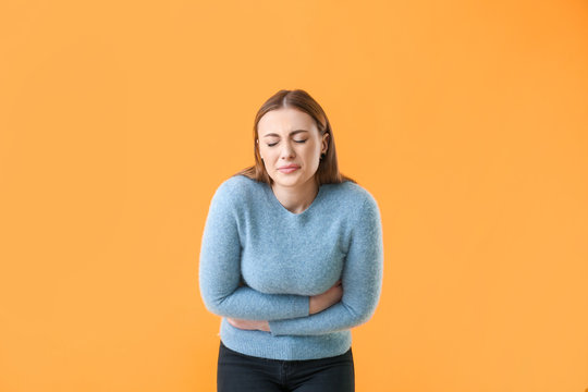 Young woman suffering from abdominal pain on color background