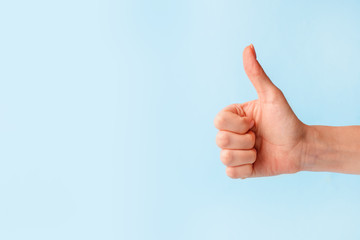 Closeup of female hand showing thumbs up sign against pastel blue background, copy space, minimal concept - 331112813