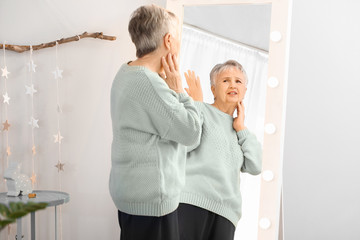 Displeased senior woman looking at her reflection in mirror