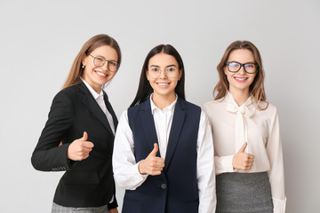 Beautiful young businesswomen showing thumb-up gesture on light background