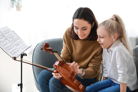 Private music teacher giving violin lessons to little girl at home