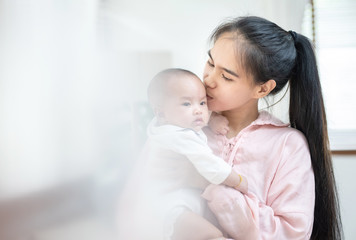 family, child and parenthood concept - happy beautiful young asian mother smiling hugging holding newborn baby in her arms at home. Mother’s day banner with copy space for advertise