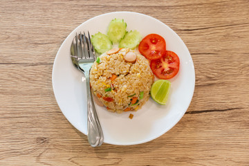 Fried rice placed on a wooden table with cucumbers and tomato