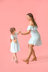 Fototapeta na wymiar Happy mother and her little daughter dancing against color background