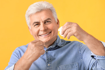 Senior man flossing teeth on color background