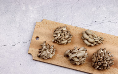 Raw oyster mushrooms served on a wooden cutting board on a light background. Top view, flat lay