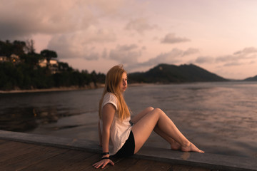 Beautiful girl at sunset on the sea in Thailand. Bright orange and yellow pink sky. Girl traveler enjoys the view. Woman in the tropics