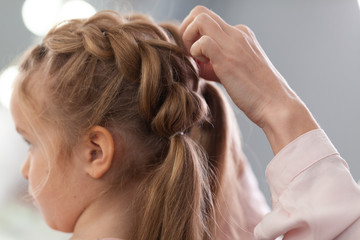 The work of the stylist on hairstyles in a bright salon, the girl makes curls and braids braids of a small beautiful model,