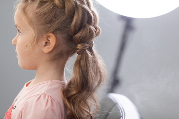 The work of the stylist on hairstyles in a bright salon, the girl makes curls and braids braids of a small beautiful model,