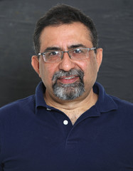 An Indian man with a goatee beard wearing spectacles against a dark background. Looking to camera - obrazy, fototapety, plakaty