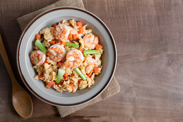 top view of stir fried egg with shrimp and vegetables in a ceramic dish on wooden table. asian homemade style food concept.
