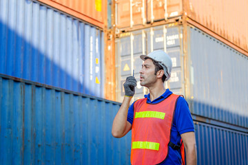 Foreman in hardhat and safety vest talks on two-way radio control loading containers box from cargo