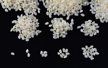 Round white grains of rice lie in exponentially increasing rice piles on a black textile surface