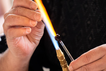 Glassblower man shaping the glass warmed by the burner flame. Close up view.