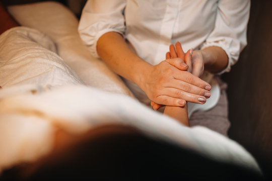 Young caucasian practicand is having a hand massage session with a woman lying on bed
