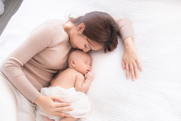 Obraz na płótnie Canvas Asian beautiful mom motherhood lie down nursing, kissing newborn baby infant toddler, gently hold together on chest with love, infant sleep comfortable with safe and protection by mother taking care