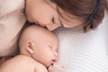 Asian beautiful mom motherhood lie down nursing, kissing newborn baby infant toddler, gently hold together on chest with love, infant sleep comfortable with safe and protection by mother taking care