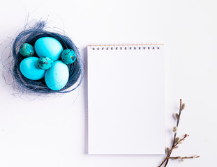 Happy easter concept. Festive spring composition blue eggs in a nest willow chistots notebook for notes white background
