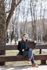 Fototapeta premium Student with glasses working on a laptop, sitting on a park bench.