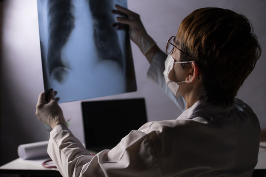 Medical doctor looking worried when inspecting x-ray film of lungs during COVID-19 pandemic outbreak crisis