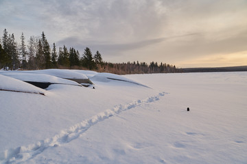     Snow- covered lake at dawn with boats on the shore.  Winter forest with snow-covered fir trees high in the mountains. Sunny February day in the spruce forest.      