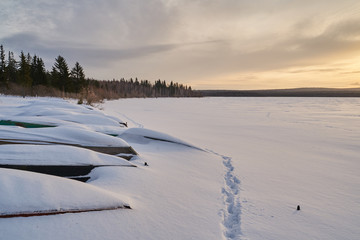     Snow- covered lake at dawn with boats on the shore.  Winter forest with snow-covered fir trees high in the mountains. Sunny February day in the spruce forest.      