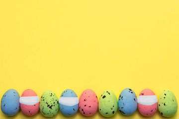 Fototapeta na wymiar Colorful easter eggs in row with virus mask on yellow background. Easter greeting card, Corona virus (COVID19) protection concepts