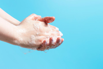 Fototapeta premium Girl washes her hands with soap close up on a blue background.