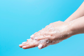 Fototapeta premium Girl carefully washes her hands with soap close-up on blue background, copy space