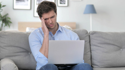 Fototapeta premium Handsome Young Man with Headache Working on Laptop while Sitting on Couch