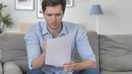 Handsome Young Man Reading Documents while Sitting on Couch