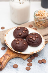 Chocolate cookies with choco drops on white plate, and glass of milk