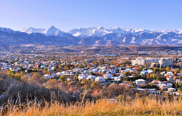 Upper part of Almaty city on the background of mountains in autumn season; first snow on the roofs of houses in golden fall, beauty and greatness of Kazakhstan concept